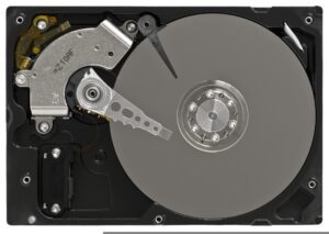 An open hard disk drive showing the circular silver disk platter, actuator arm, and read/write head inside a black rectangular casing—ideal for secure electronics recycling or Omaha electronics recycling services.